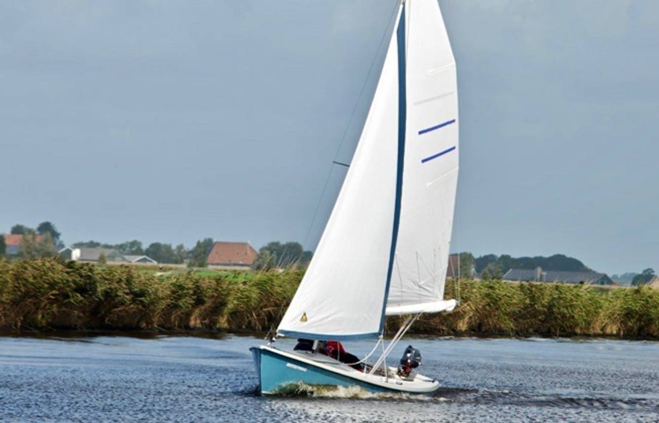 Zeilboot onder vol zeil langs de rietkraag